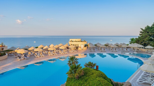 A resort pool with sun loungers and umbrellas, a building with a circular design, and a view of the sea. - Melas Resort Hotel (Manavgat)