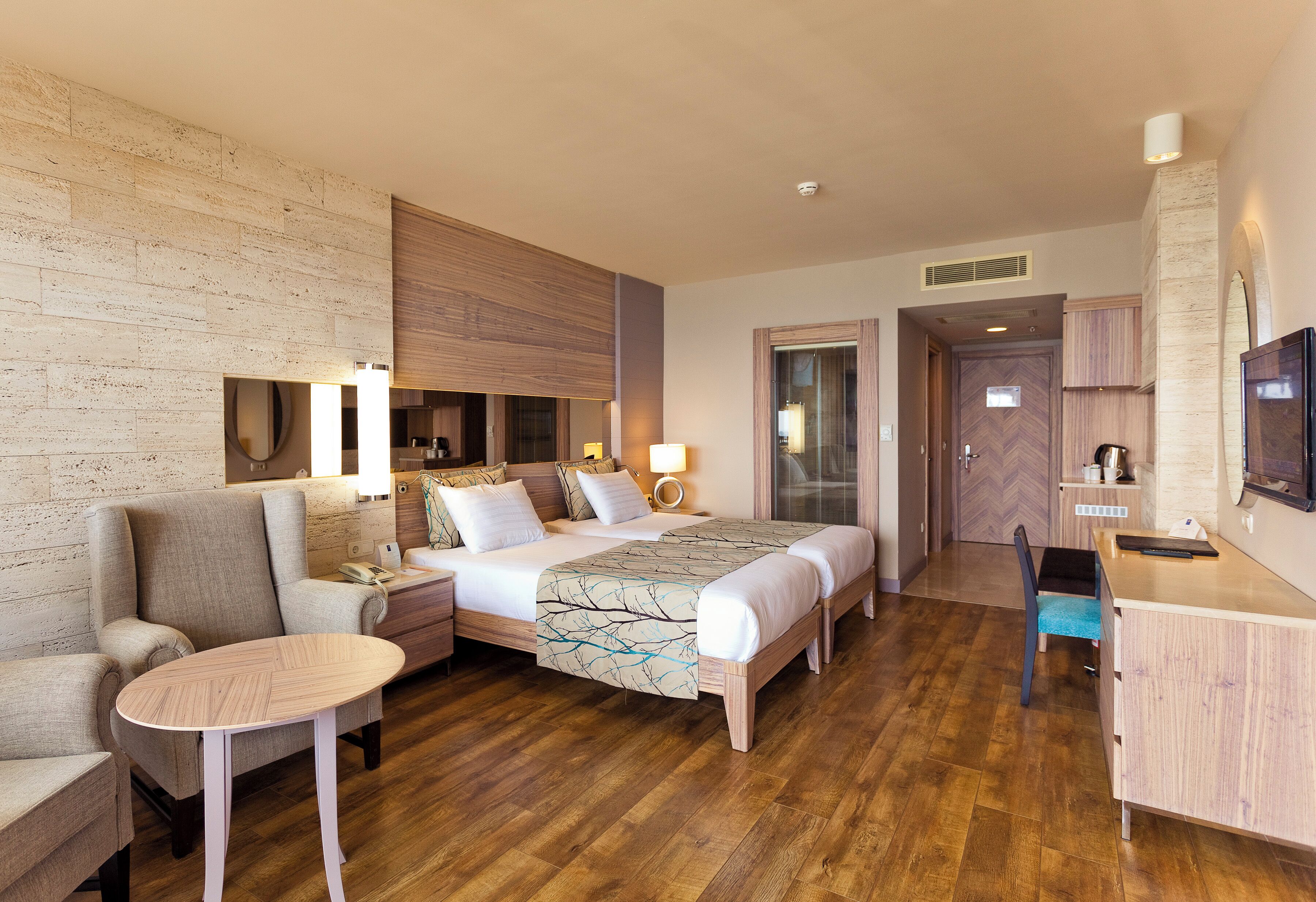 A hotel room with a bed, a desk, a chair, a small table, a sofa, and a TV.