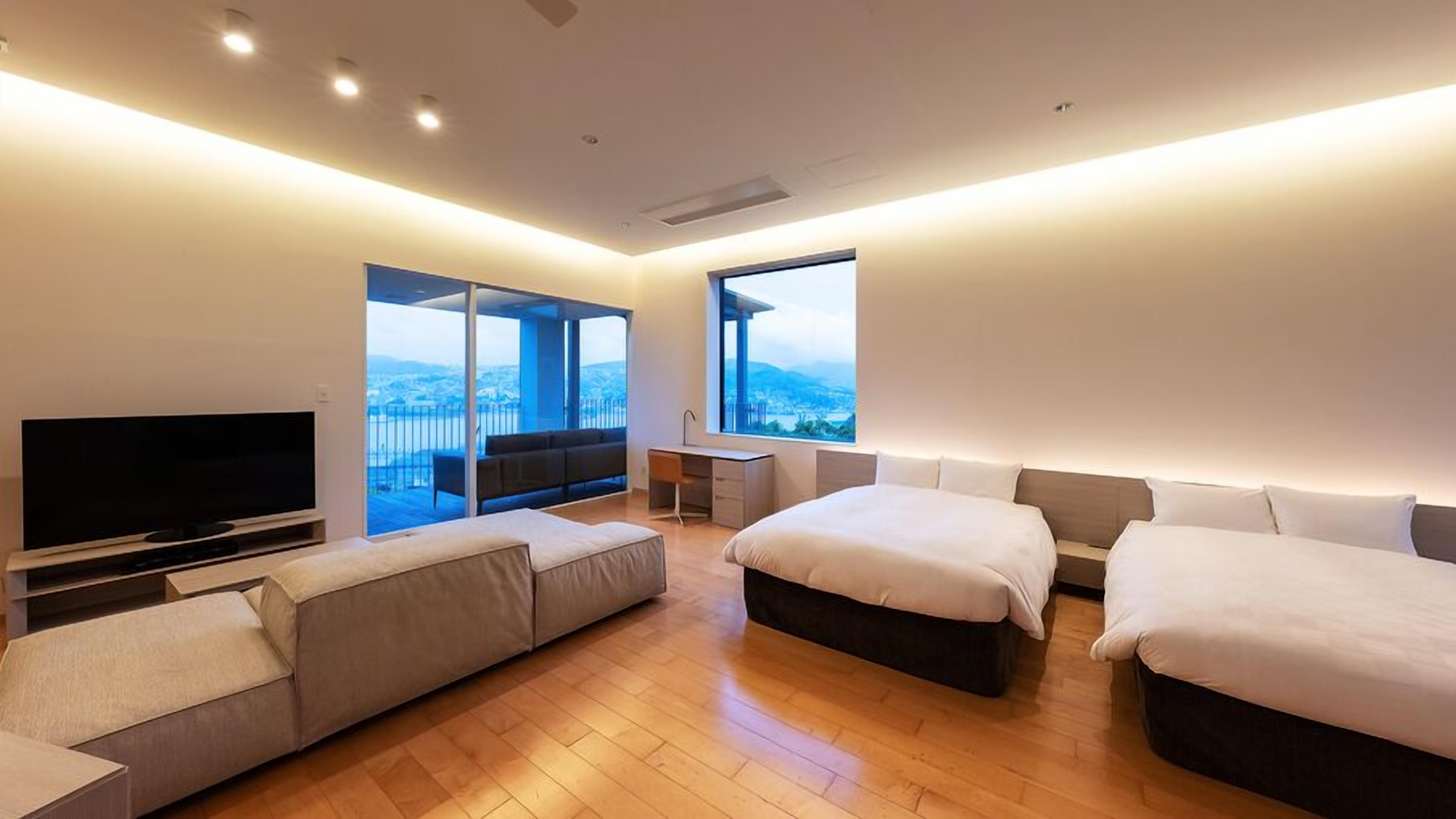 A modern hotel room with a large bed, a sofa, a desk, and a TV.