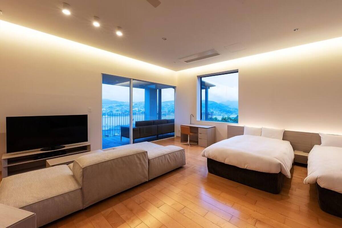 A modern hotel room with a large bed, a sofa, a desk, and a TV.