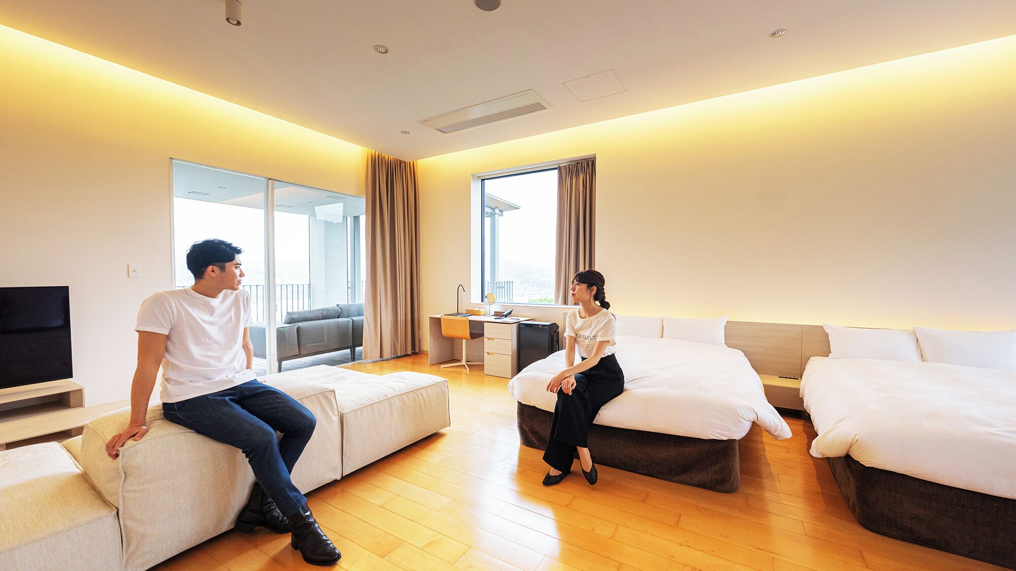 A hotel room with a sofa, two beds, a desk, and a TV.