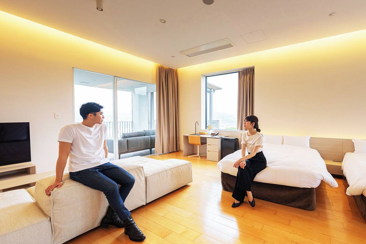A hotel room with a sofa, two beds, a desk, and a TV.