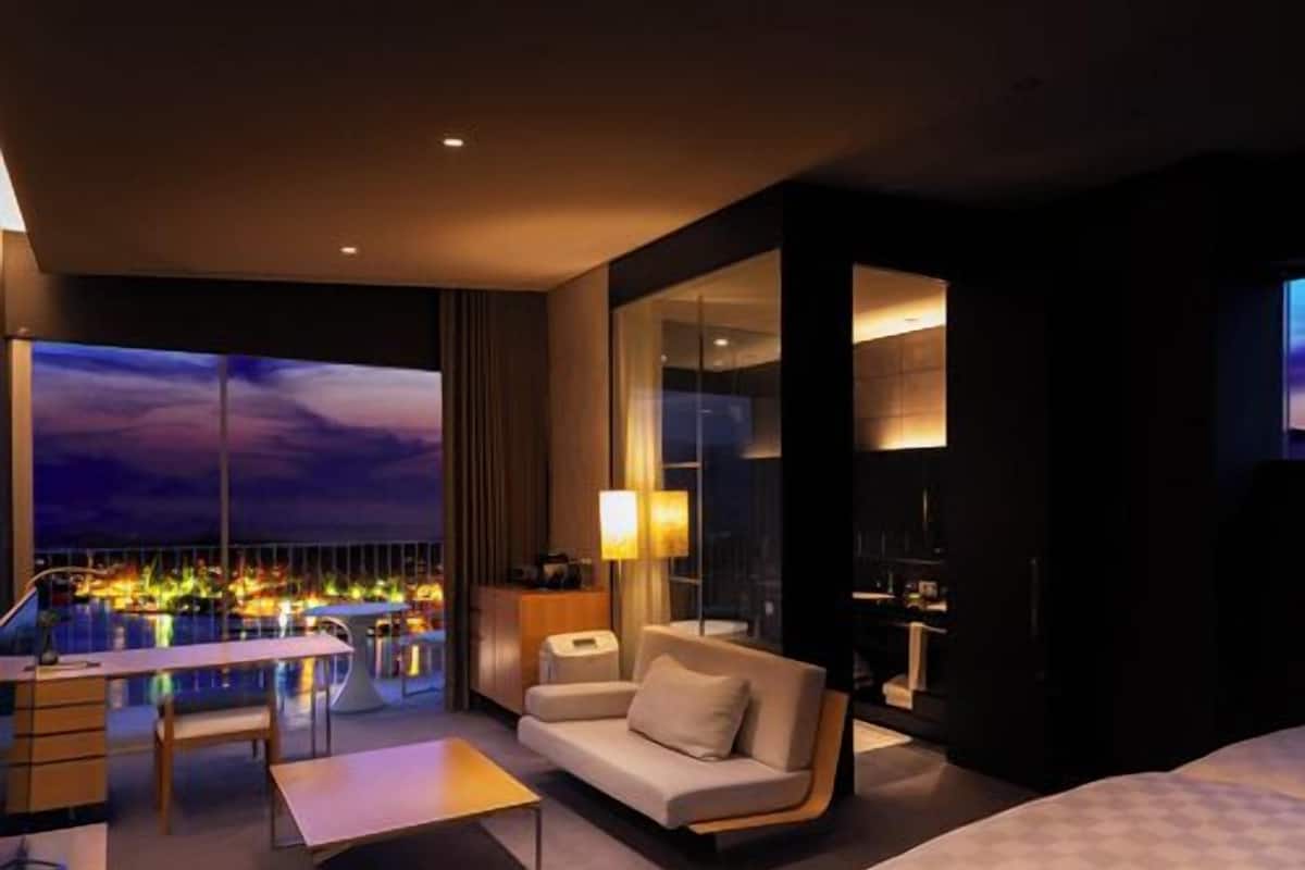 A hotel room with a bed, a sofa, a desk, and a balcony with a city view.