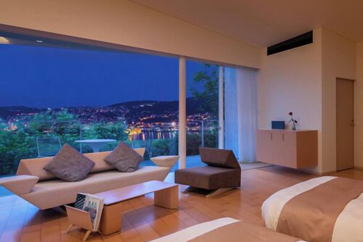 A modern bedroom with a large window, a sofa, a chair, and a bed.