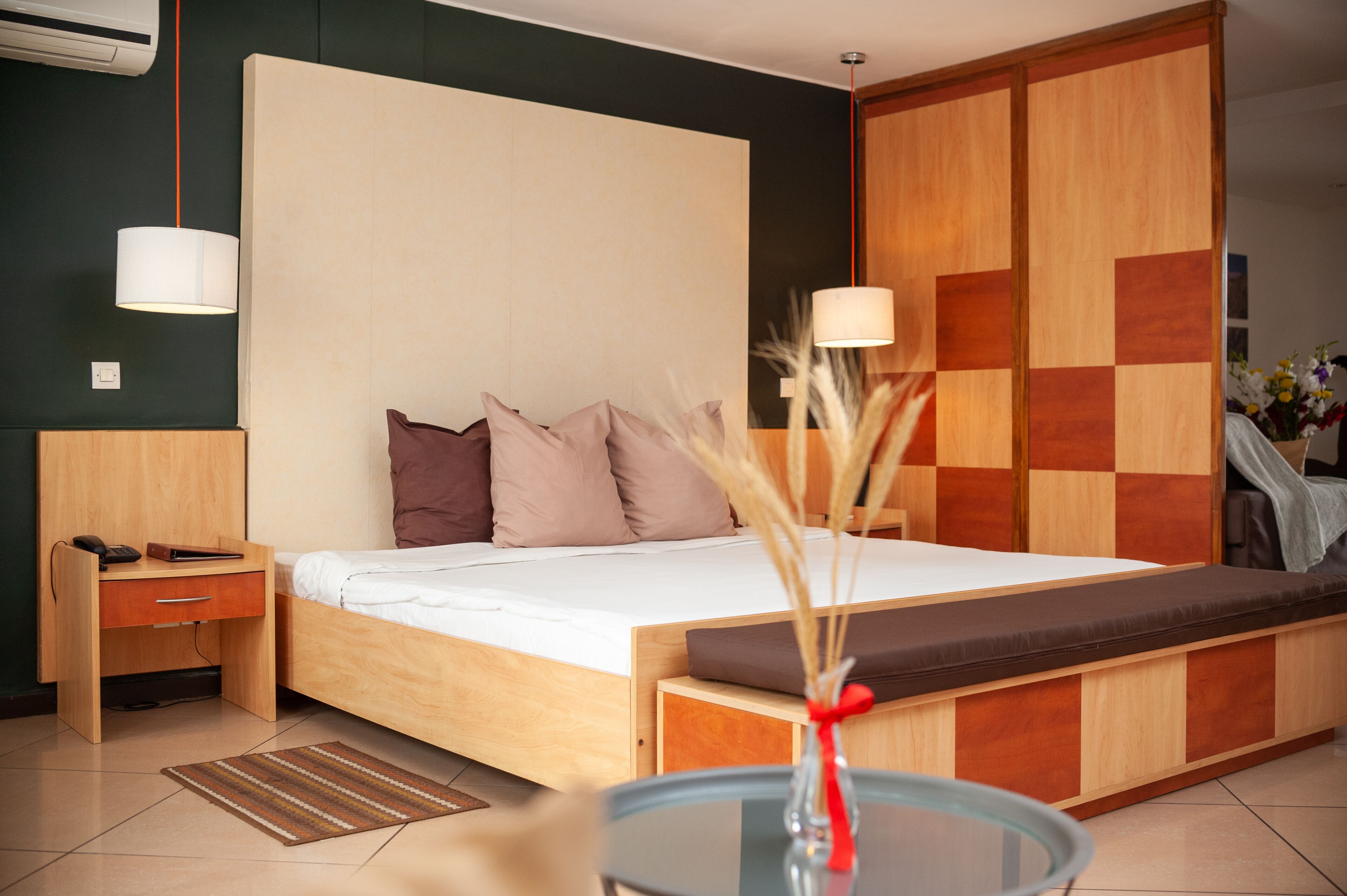 A modern bedroom with a wooden bed, a bedside table, a lamp, and a vase with dried plants.