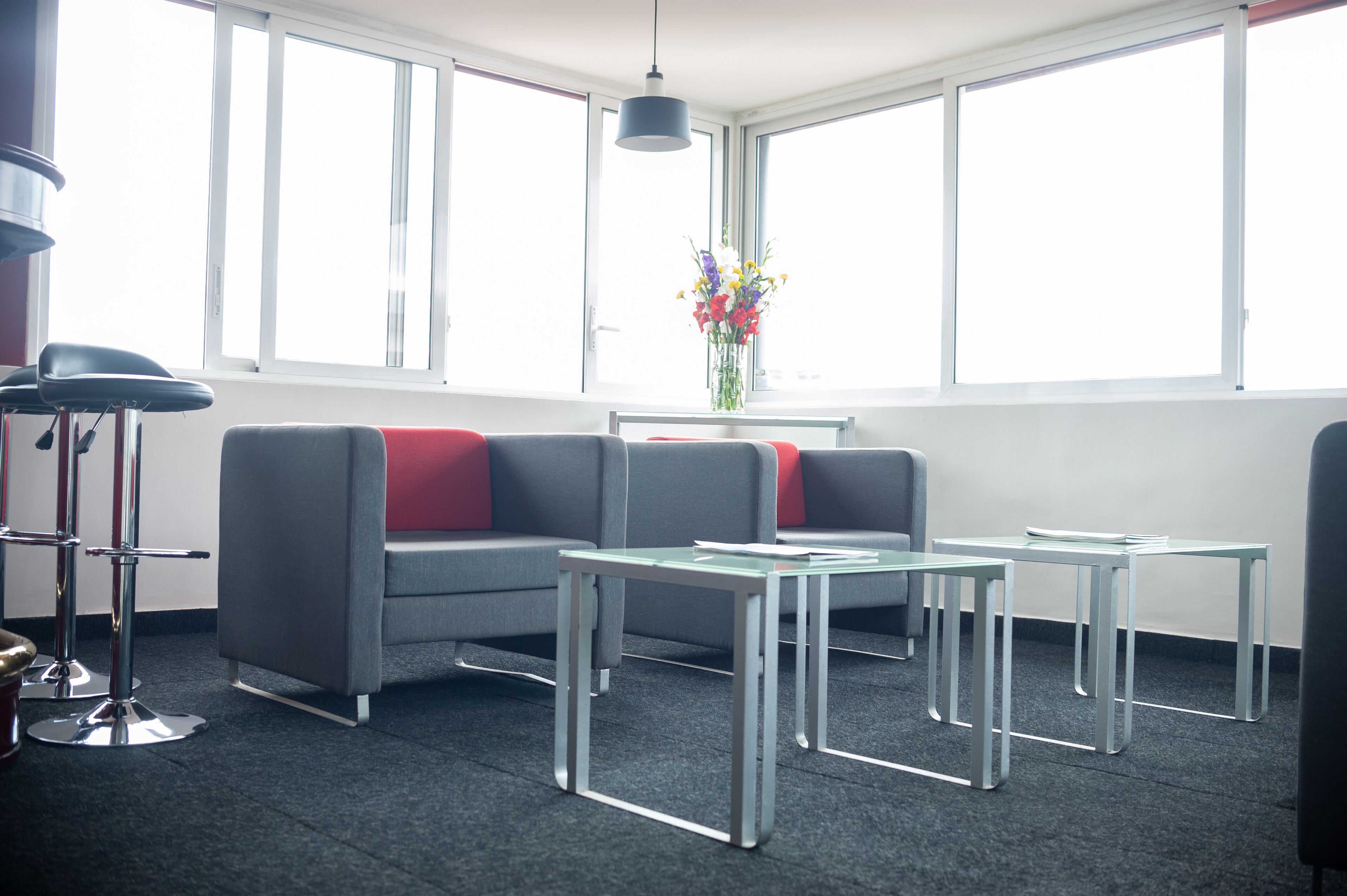 Un espace de bureau moderne avec un canapé gris, des coussins rouges et une table en verre.