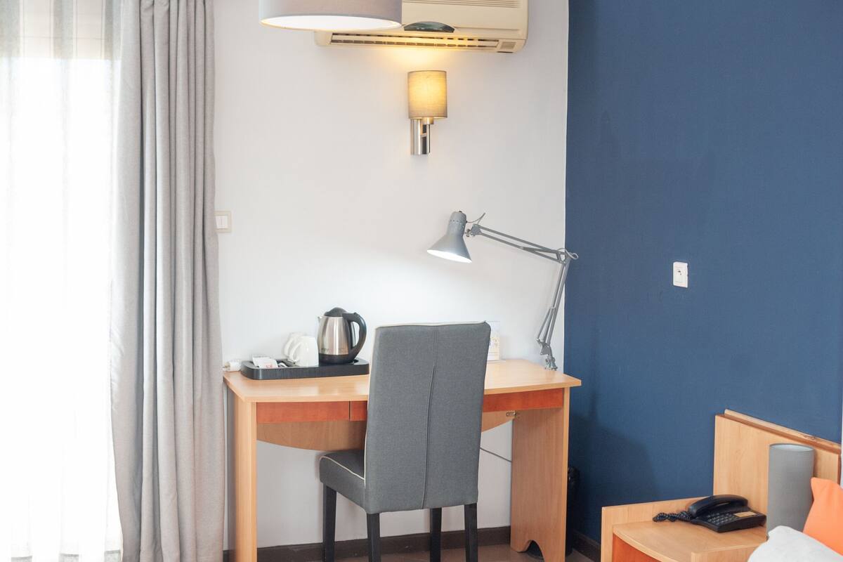A hotel room with a bed, a desk with a chair, a lamp, a phone, and a coffee maker.