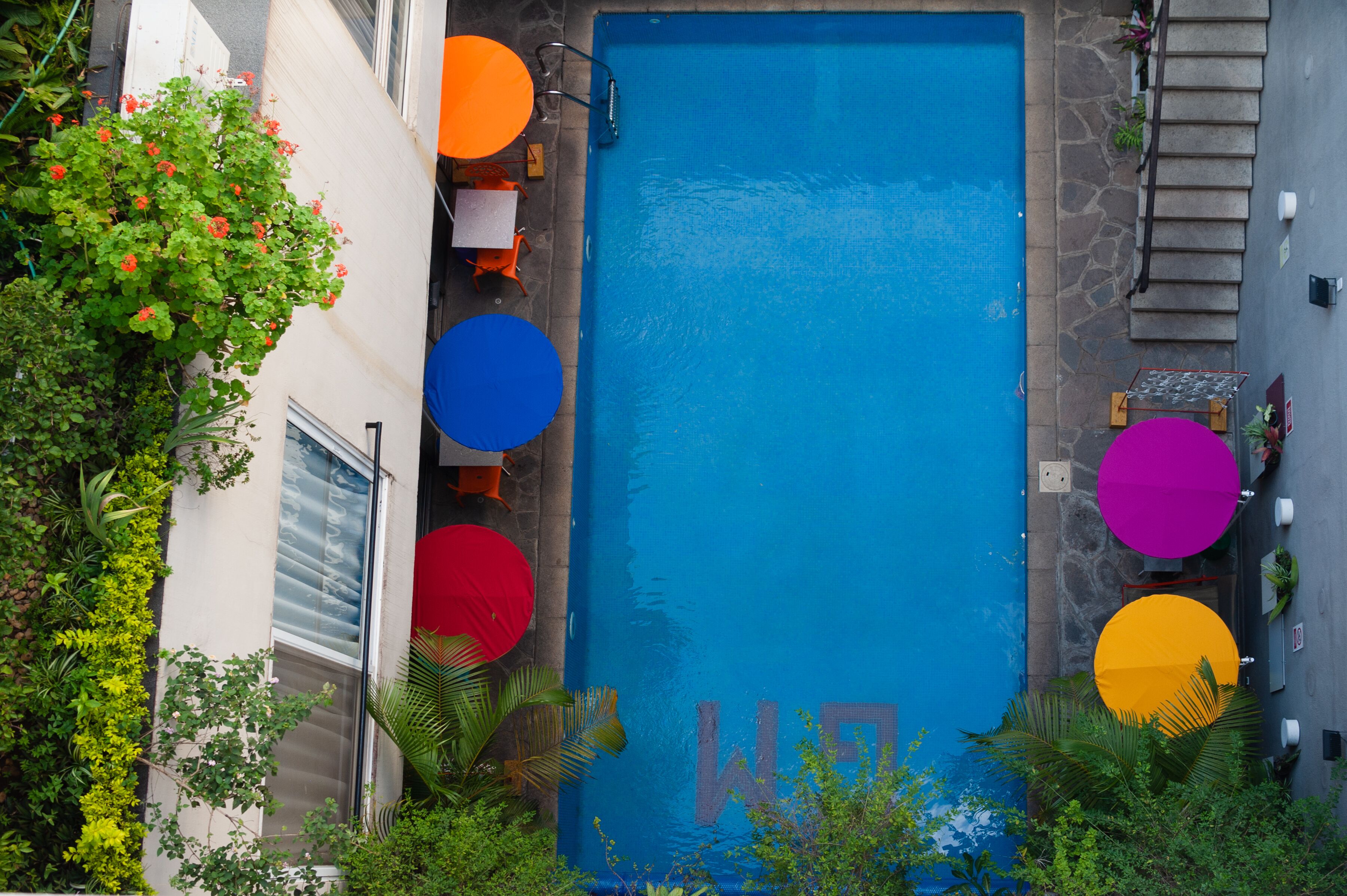 A rooftop pool with a blue water feature, surrounded by colorful umbrellas and chairs.