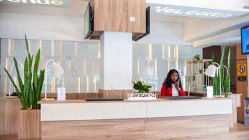 A reception desk with a 'RECEPTION' sign, a TV screen, and potted plants.