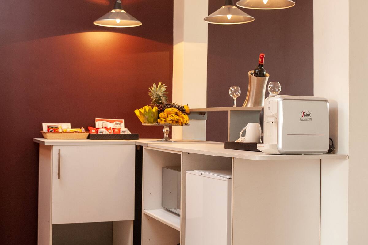 A compact kitchen with white cabinets, a coffee machine, and two pendant lights.