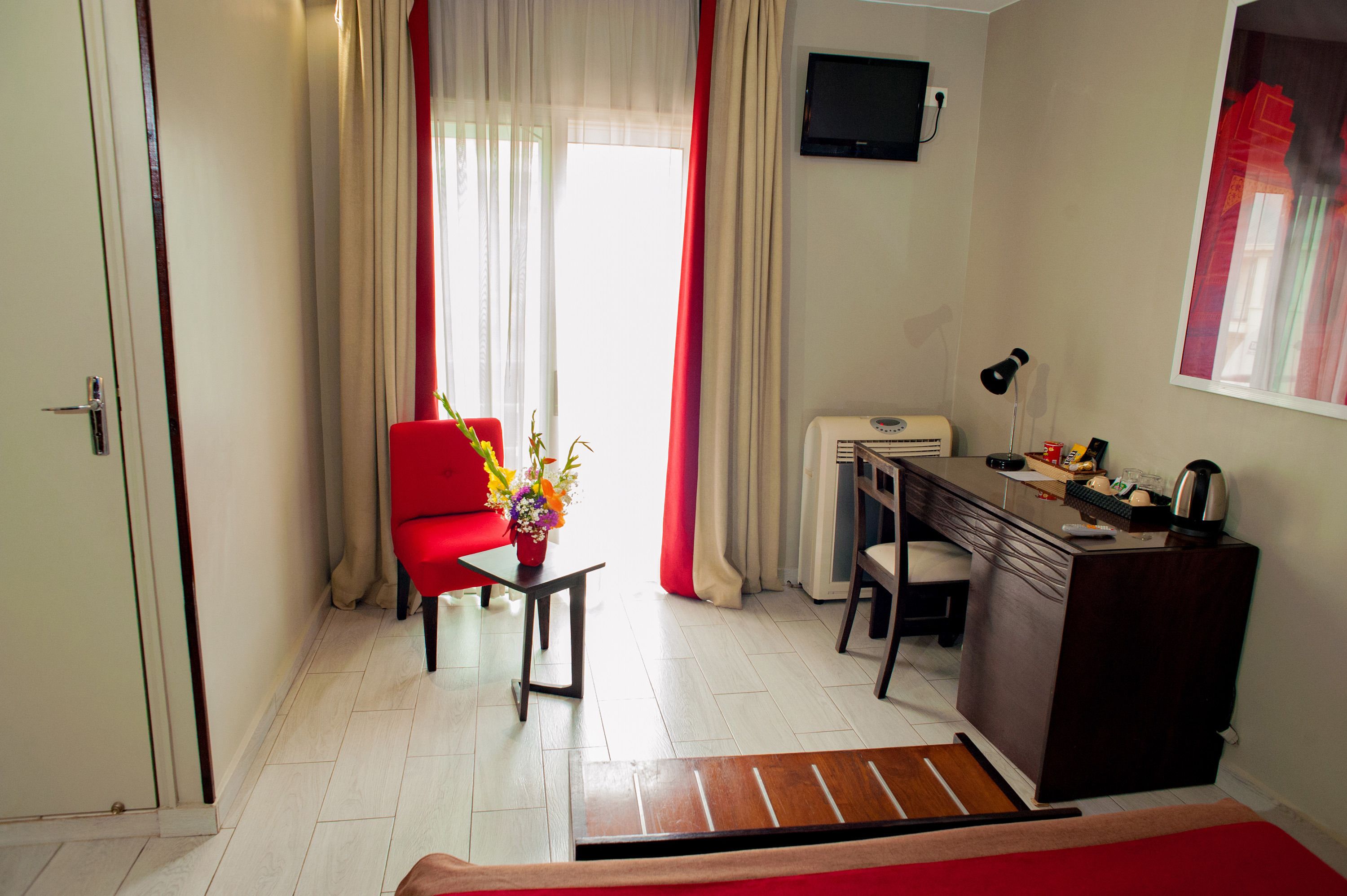 Ein Hotelzimmer mit Schreibtisch, Stuhl und einem kleinen Tisch mit Blumen in einer Vase.
