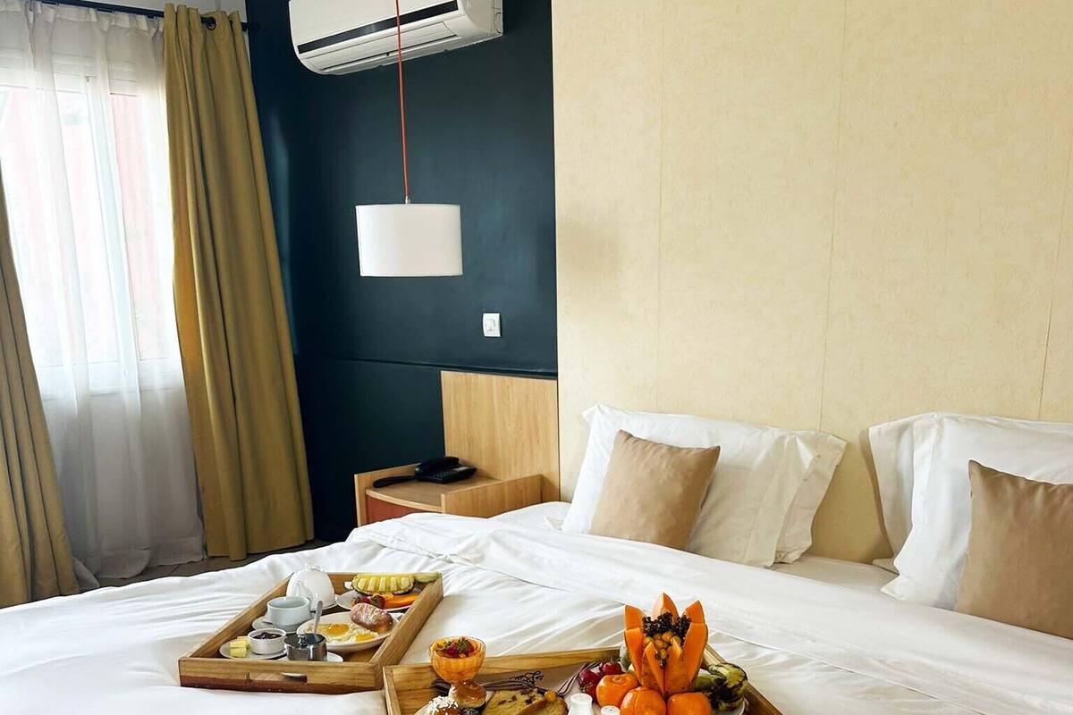 A hotel room with a large bed, a bedside table, an air conditioning unit, and a window with curtains.