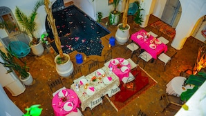 An indoor dining area with multiple tables set for a meal, surrounded by potted plants and a central water feature. - Riad El Kenz (Marrakech)