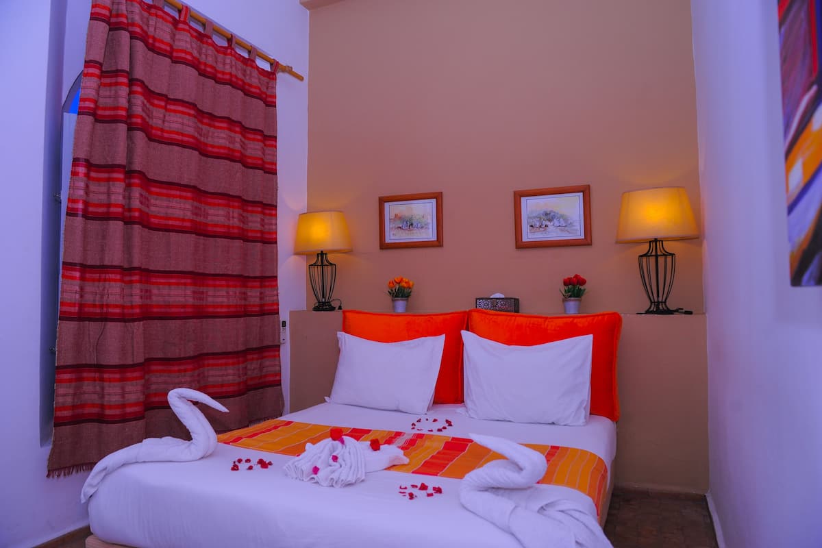 A hotel room with a bed, two wall-mounted lamps, two framed pictures, and a curtain.