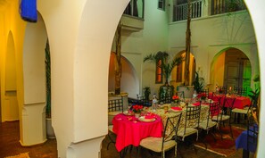 Comedor con varias mesas dispuestas para una comida, rodeado de arcos y plantas en macetas.