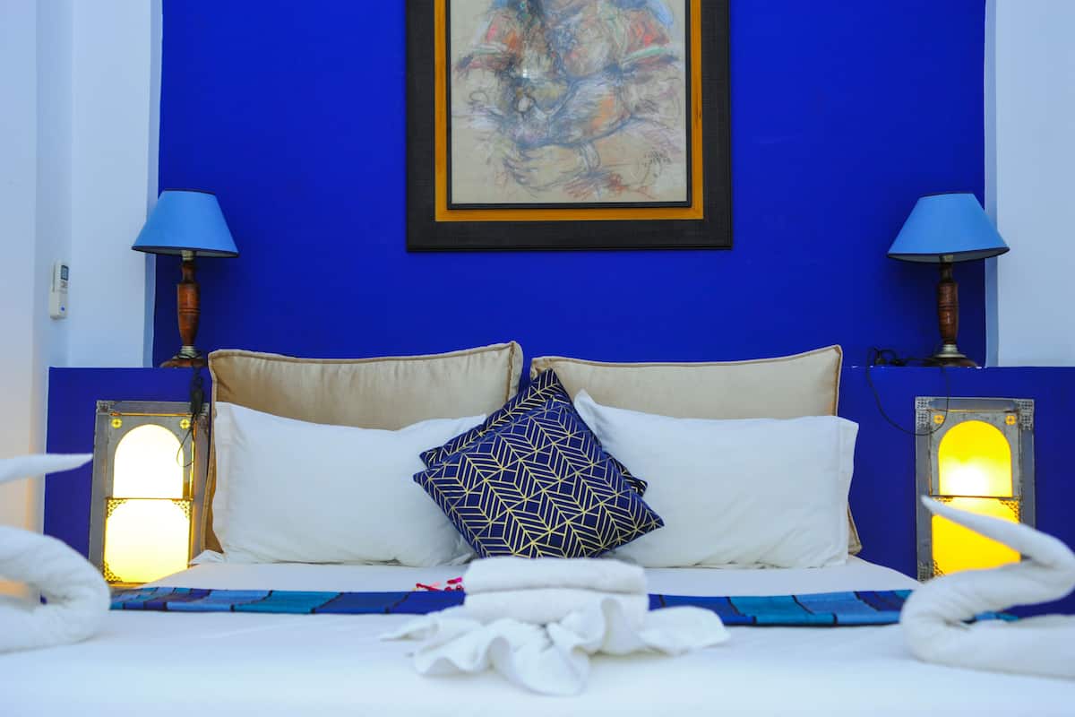 A bed with white linens, a blue and gold patterned pillow, and two wall-mounted lamps.