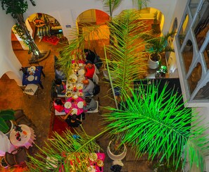 An indoor dining area with tables set for a meal, surrounded by potted plants and architectural arches. - Riad El Kenz (Marrakech)