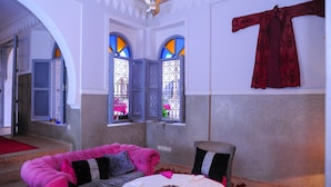 A room with a pink sofa, a round table, and a red curtain on the wall. - Riad El Kenz (Marrakech)
