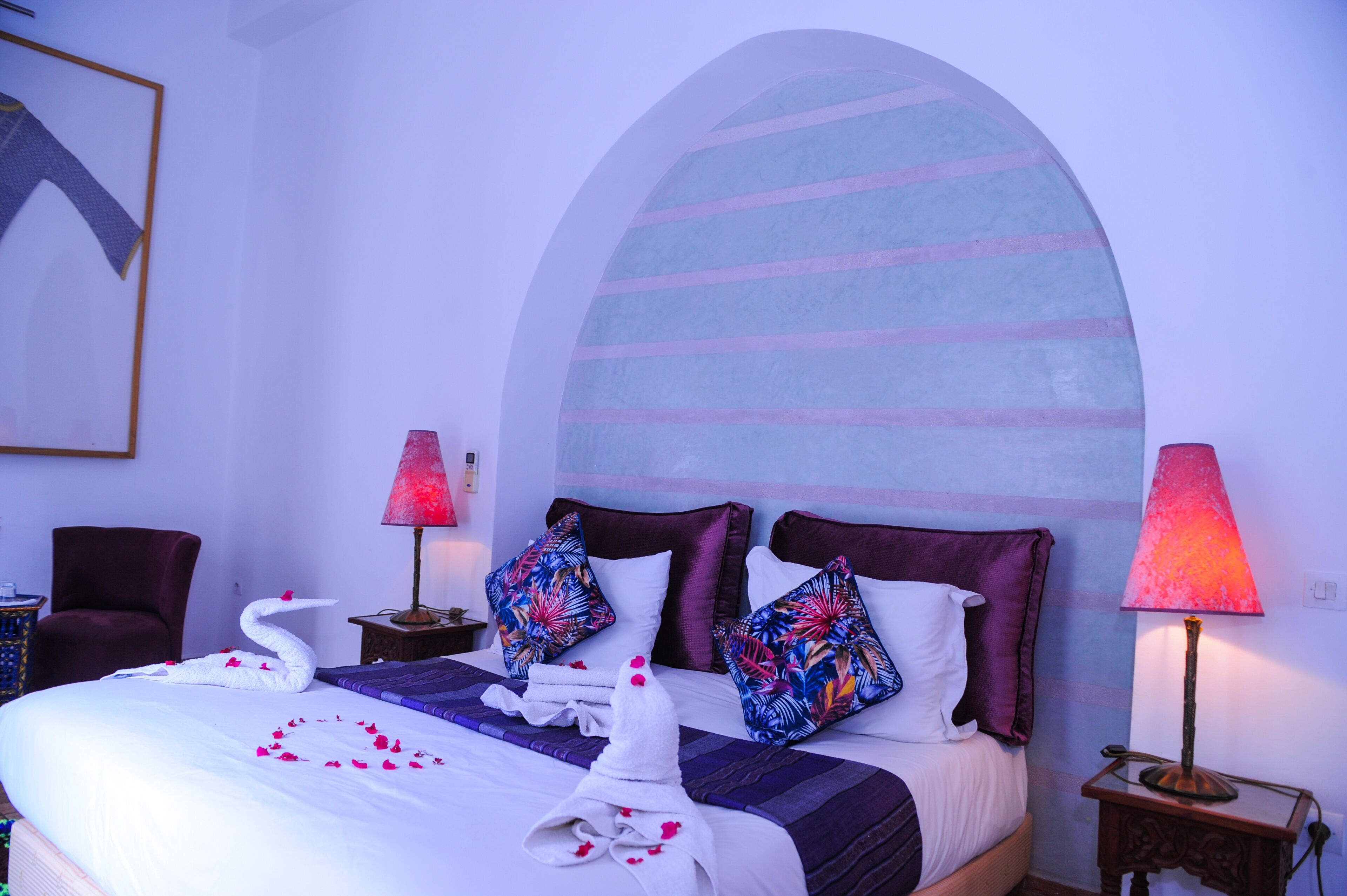 Ein Hotelzimmer mit einem Bett, zwei Nachttischen, einem Sessel und einem großen Bogenfenster.