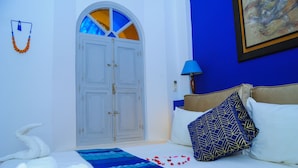 A hotel room with a bed, a blue and white patterned bedspread, a white towel, a blue lamp, and a painting on the wall. - Riad El Kenz (Marrakech)