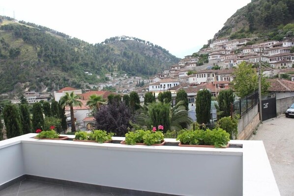 Uma varanda com plantas em vasos e vista para uma vila na encosta, com edifícios.