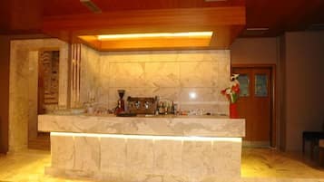 A bar area with a marble countertop, a coffee machine, and a vase with flowers.