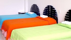 Drei Einzelbetten mit verschiedenfarbiger Bettwäsche, ein kleiner Nachttisch und eine Wandleuchte.