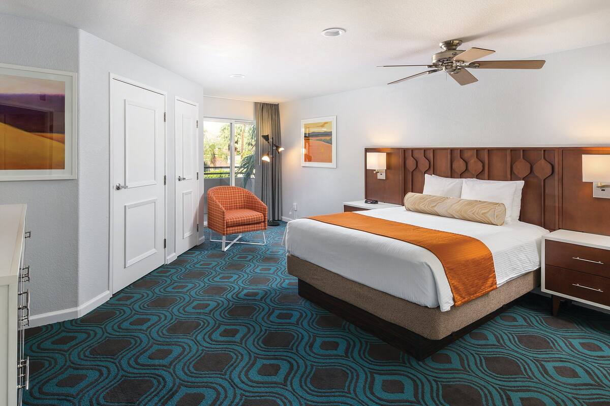 A hotel room with a bed, a chair, a desk, and a ceiling fan.
