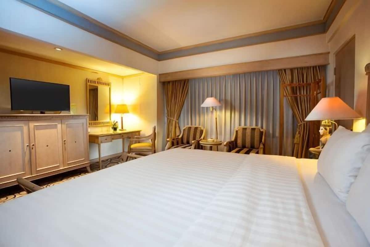 Una habitación de hotel con una cama grande, un escritorio con una silla, un televisor y dos lámparas.