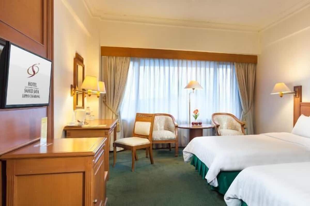 Habitación de hotel con dos camas, un escritorio, una silla, una lámpara y una ventana con cortinas.