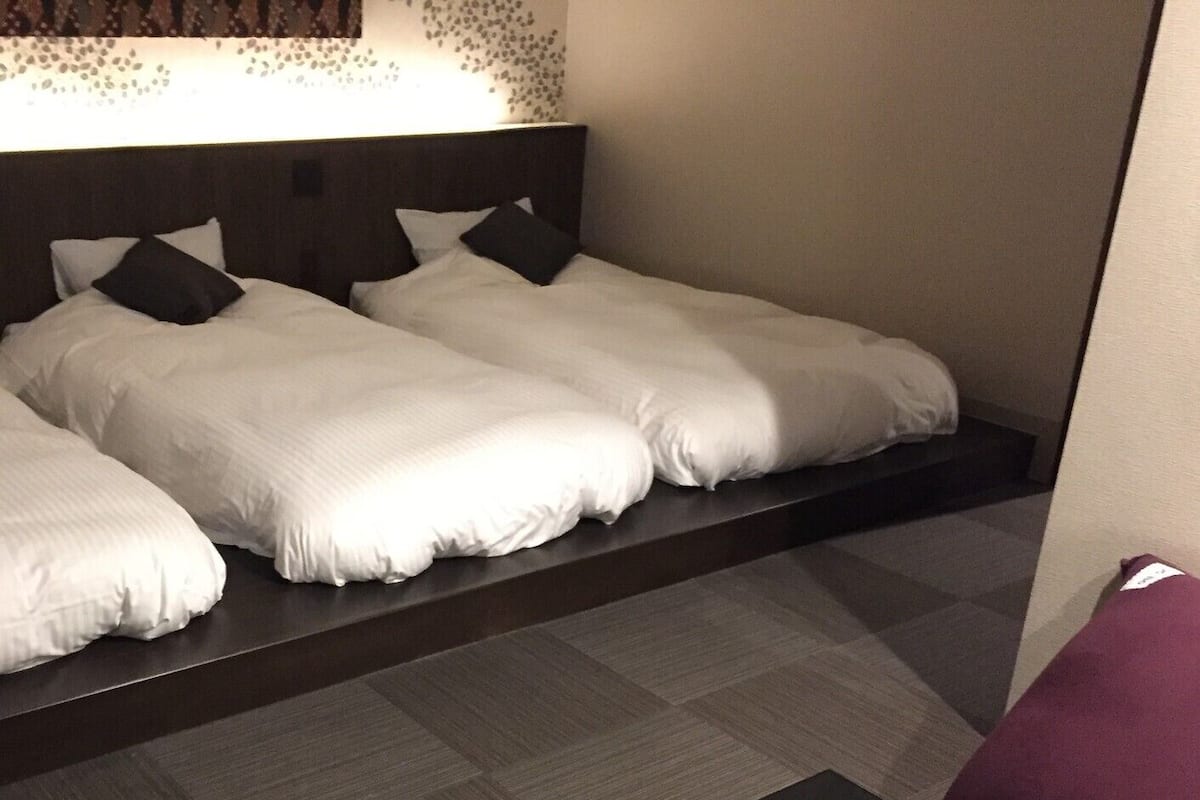 Una habitación de hotel con dos camas, una mesita pequeña y un banco.