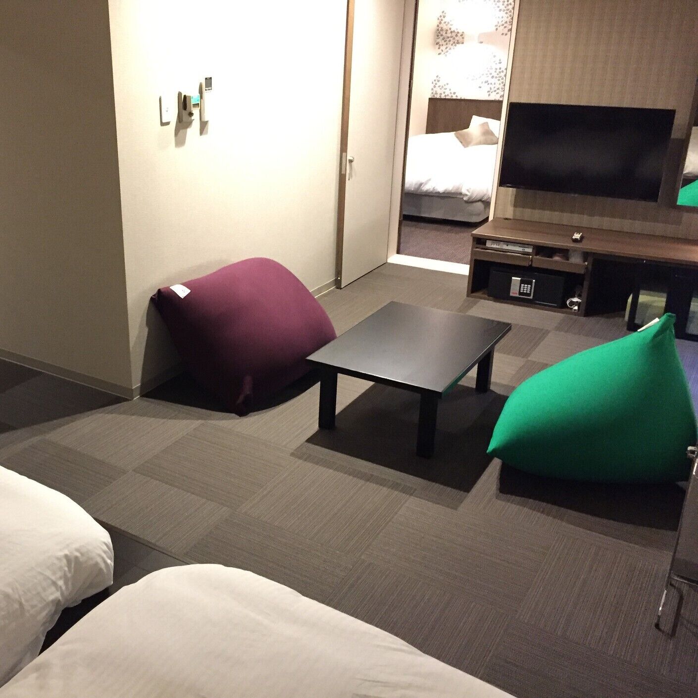 A hotel room with a bed, a TV, a small table, and two bean bags.