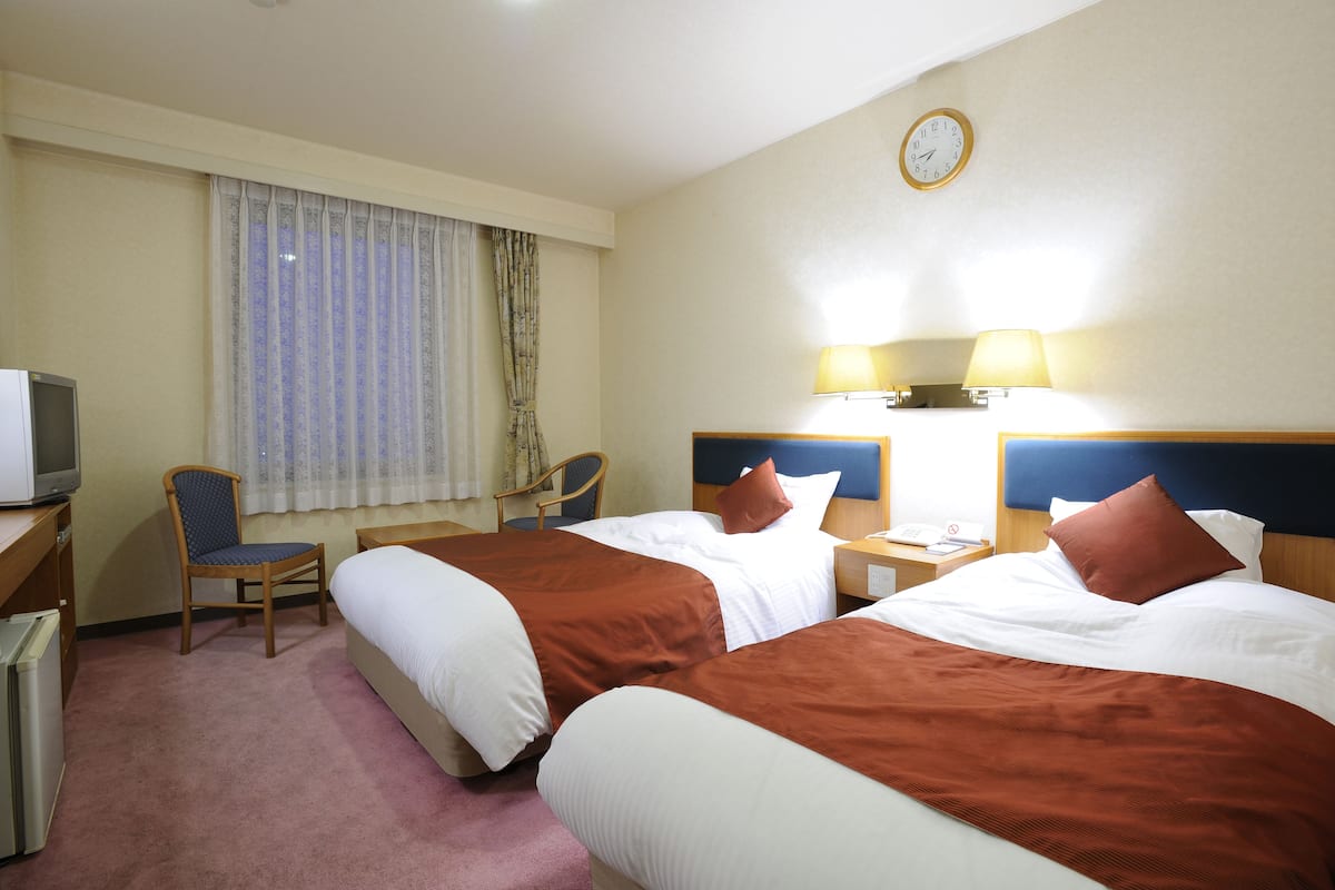 Habitación de hotel con dos camas, televisión, una silla, un escritorio y un reloj en la pared.