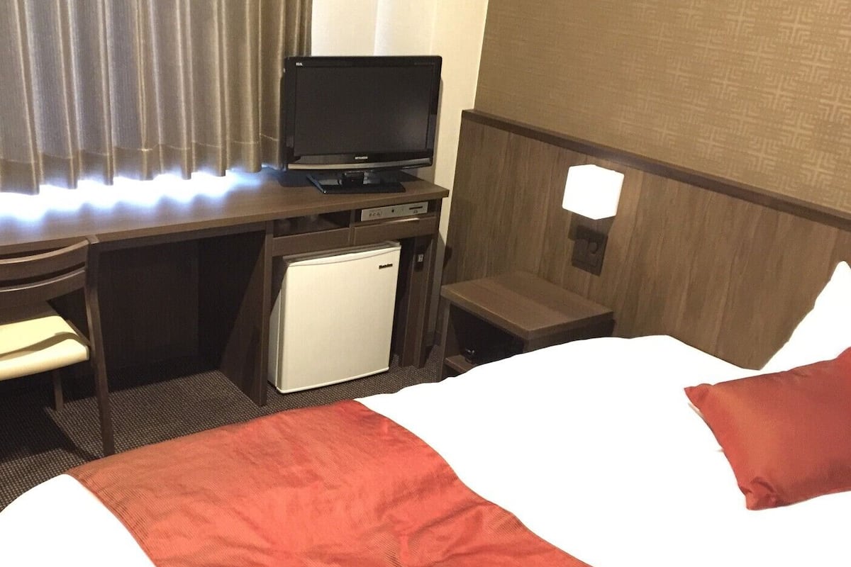 Habitación de hotel con cama, escritorio con televisor, refrigerador pequeño y mesita de noche.