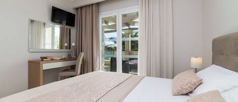 Quarto de hotel com cama, escrivaninha, cadeira, televisão e janela com cortinas.