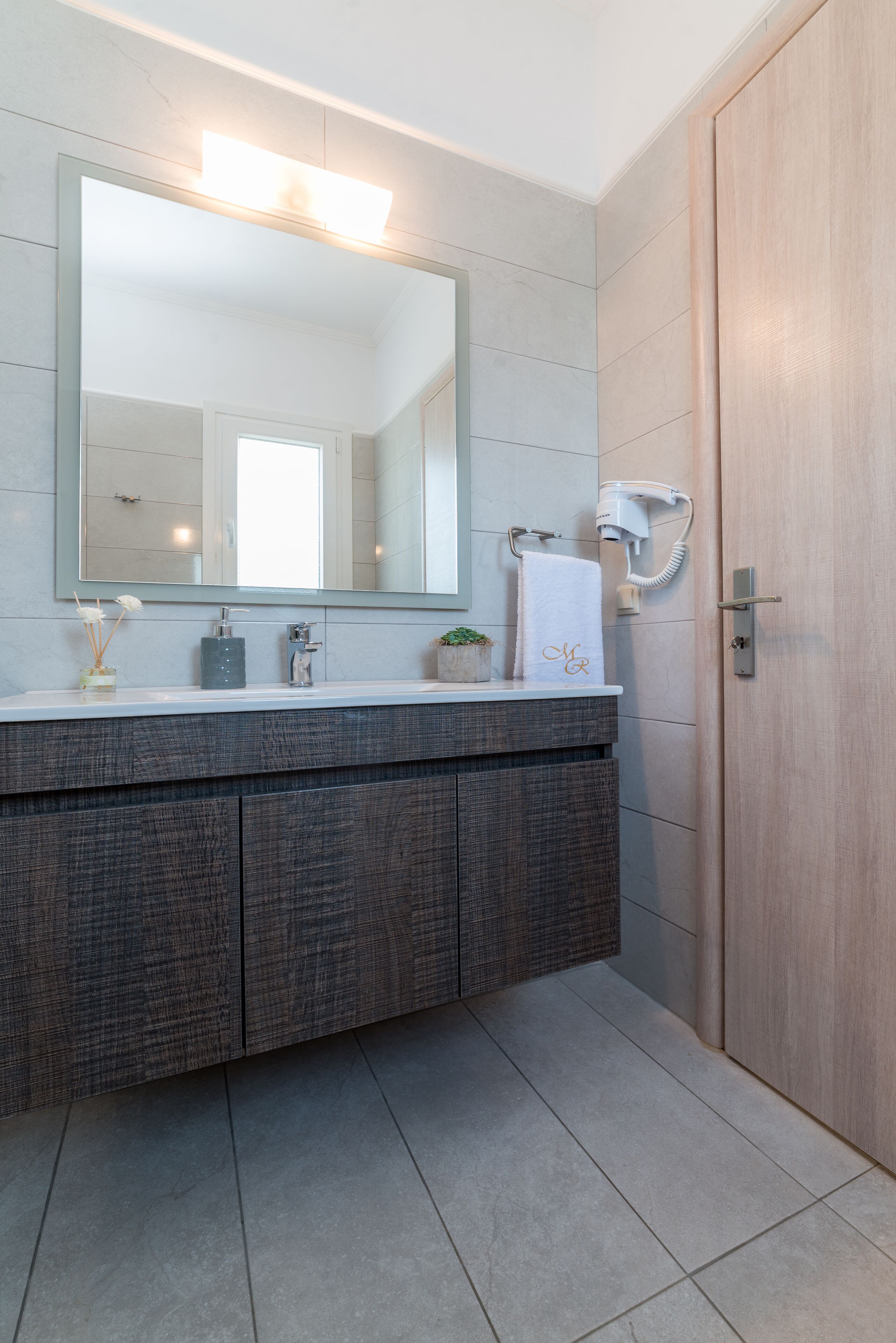 A modern bathroom with a large mirror, a white sink, a towel, and a hairdryer.