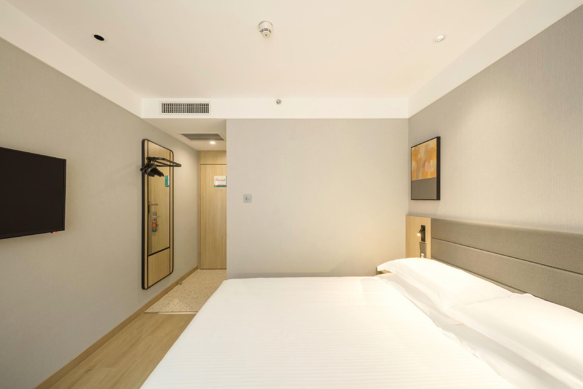 Ein modernes Hotelzimmer mit einem großen Bett, einem flachbildfernseher an der Wand, einem begehbaren Kleiderschrank und einer Tür zum Badezimmer.