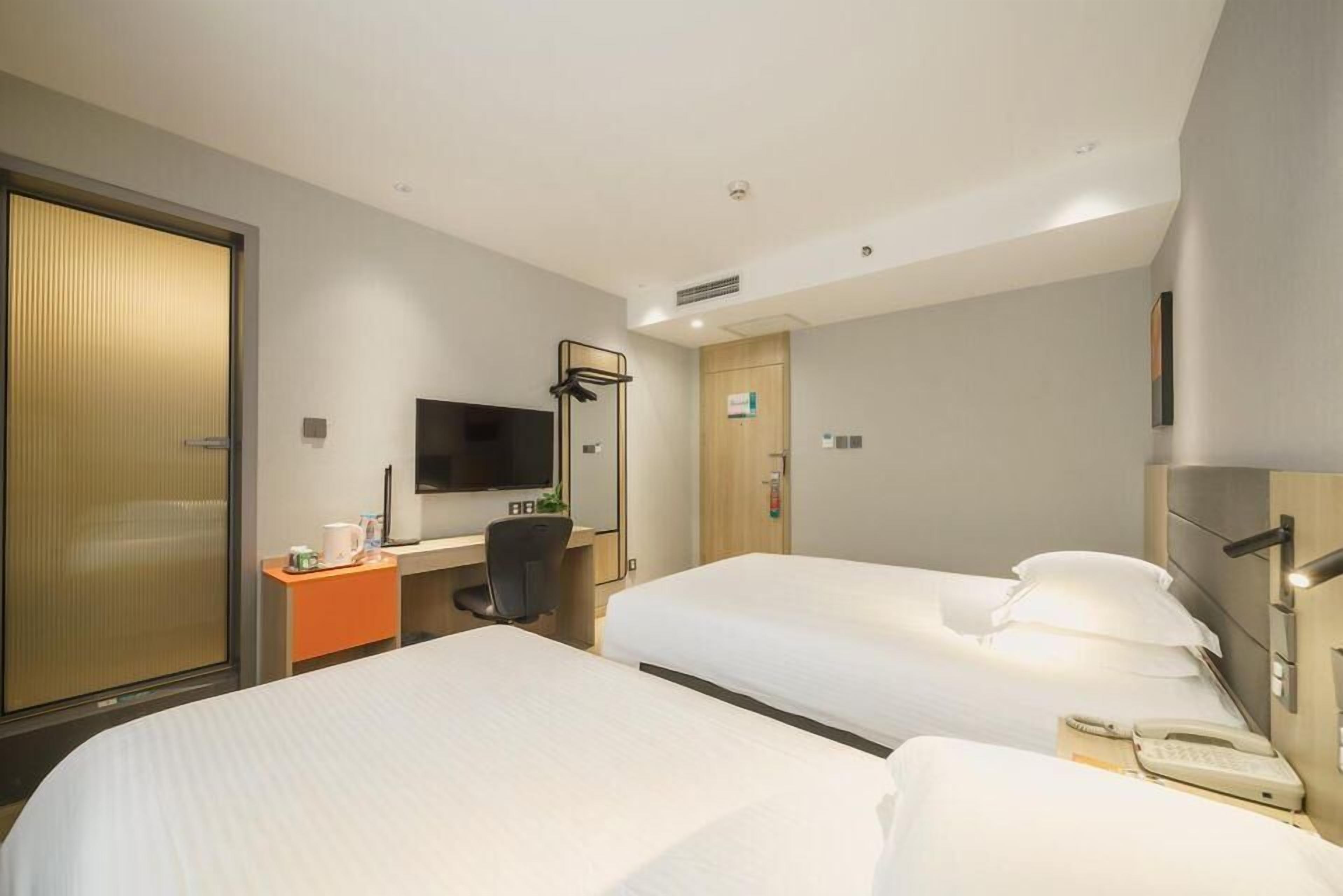 Ein Hotelzimmer mit zwei Betten, einem Schreibtisch mit Stuhl, einem Fernseher und einer Minibar.