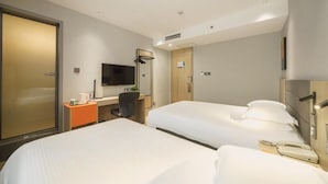 A hotel room with two beds, a desk with a chair, a TV, and a minibar.