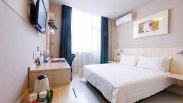 Habitación de hotel con cama, escritorio con silla, televisor montado en la pared y ventana con cortinas.