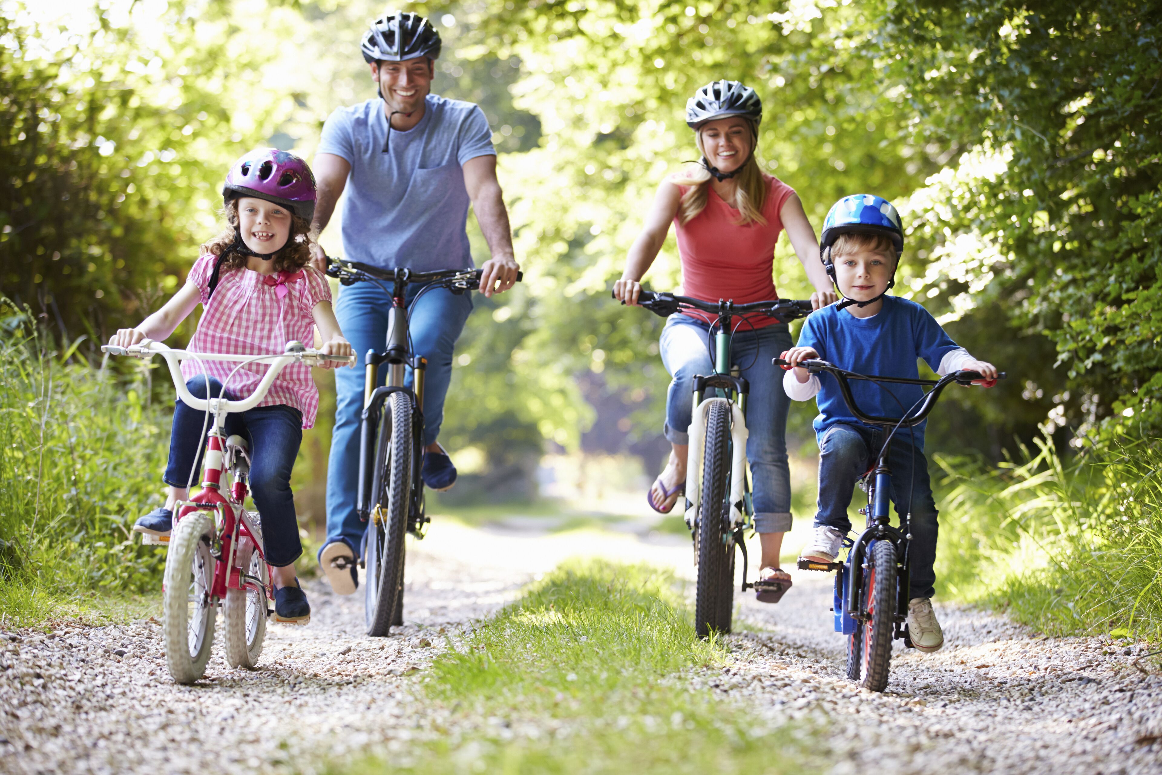 A family of four on bicycles on a gravel path surrounded by greenery.