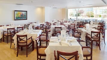 A restaurant with multiple tables set for dining, wooden chairs, and a large window offering a view of the outside.
