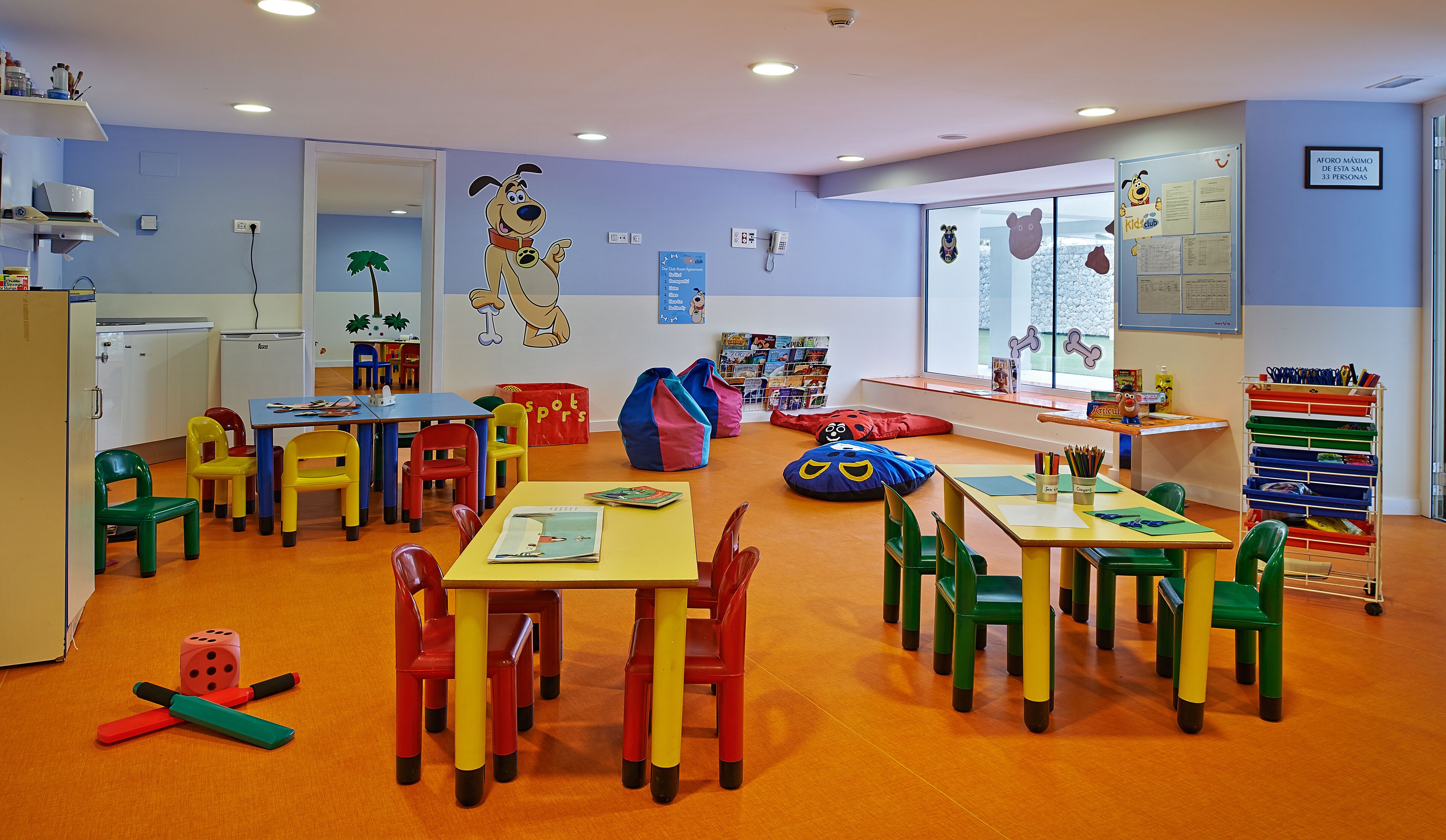 A children's playroom with colorful furniture, a large cartoon mural, and educational materials.
