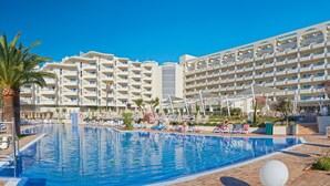 Un hotel con una piscina grande, varios balcones y tumbonas.