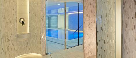 Un interno moderno con una parete curva, una porta in vetro che dà su una zona piscina e un pavimento in marmo.