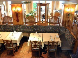 Un restaurante con mobiliario de madera, un banco floral y mesas preparadas para comer.