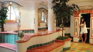 A hotel lobby with a colorful checkered floor, a curved staircase, and a large potted plant. - Lukasmayr Hotel (Bruck an der Grossglocknerstrasse)