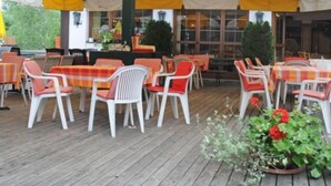 An outdoor patio with wooden flooring, white plastic chairs, and yellow and white striped tablecloths. - Lukasmayr Hotel (Bruck an der Grossglocknerstrasse)