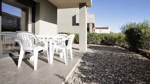 A patio with a table and chairs, a gravel area, and a building with a tiled roof in the background. - Casas Adosadas Romani (Mont-roig del Camp)