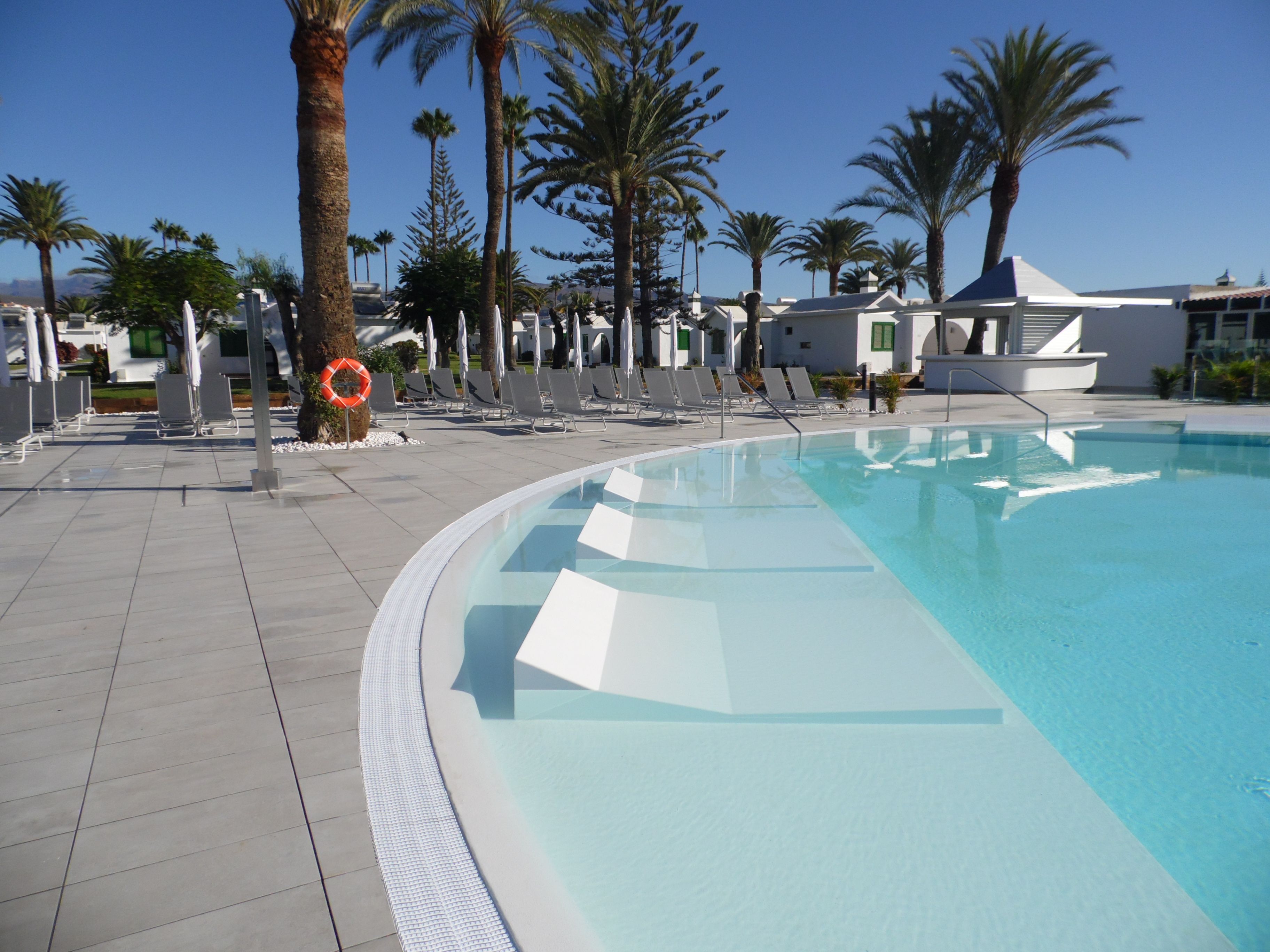 A swimming pool with lounge chairs and palm trees.
